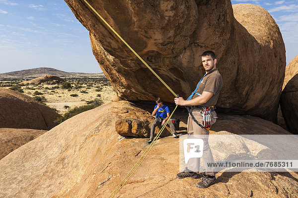 Young man hanging in a climbing rope  Bogenfels  Spitzkoppe area  Namibia  Africa
