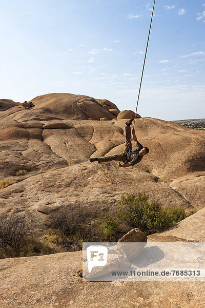 Junger Mann hängt im Kletterseil  Bogenfels  Spitzkoppe-Gebiet  Namibia  Afrika