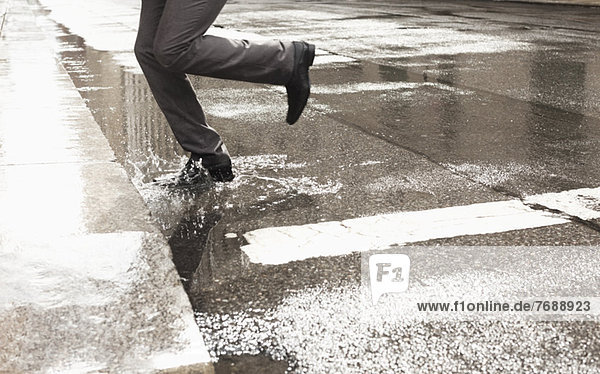 Businessman stepping in puddle on city street