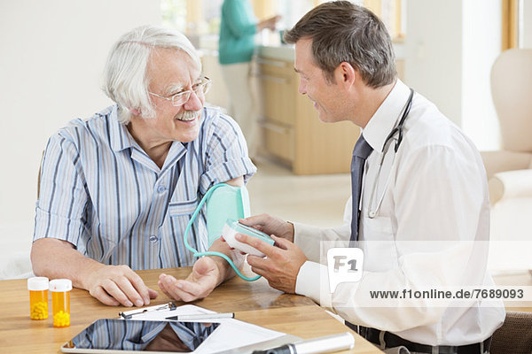 Arzt  der den Blutdruck eines älteren Patienten beim Hausbesuch testet.
