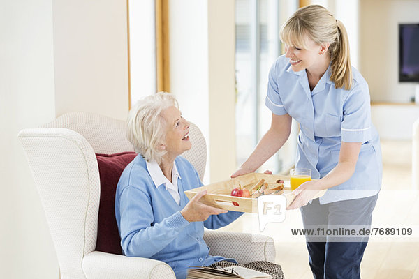 Betreuerin gibt älteren Frauen Tablett mit Lebensmitteln