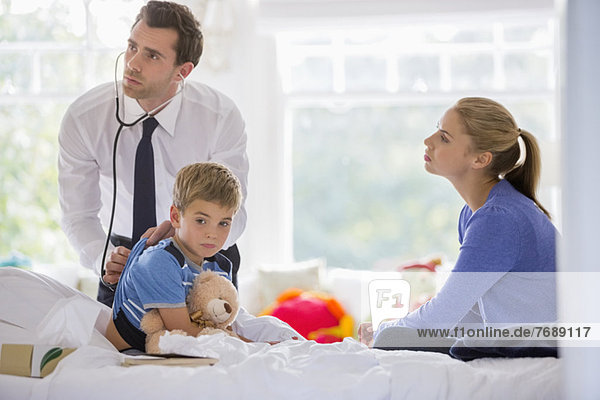 Doctor listening to boy's heartbeat at house call