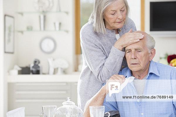 Ältere Frau fühlt sich auf der Stirn ihres Mannes krank.