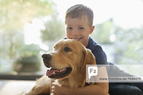 Lächelnder Junge umarmt Hund im Haus