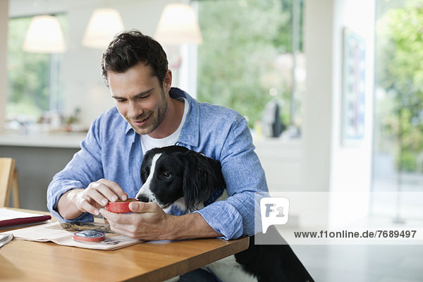 Mann füttert Hund am Küchentisch
