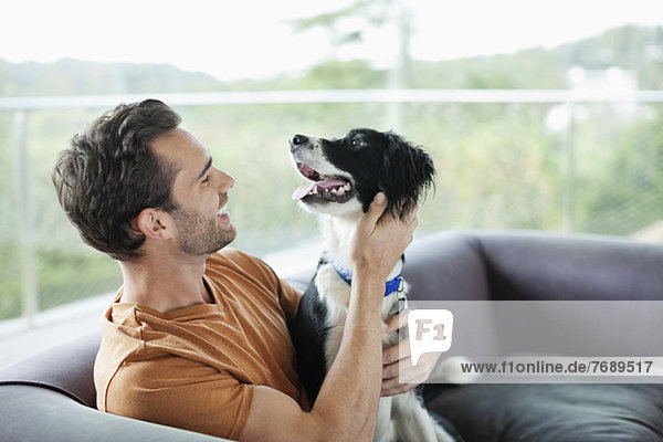 Smiling man petting dog on sofa