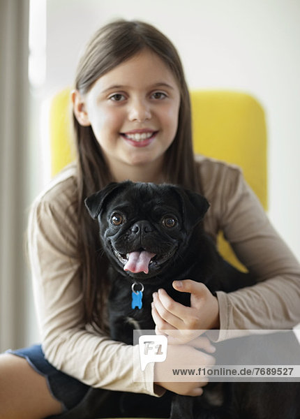 Lächelndes Mädchen hält Hund im Haus