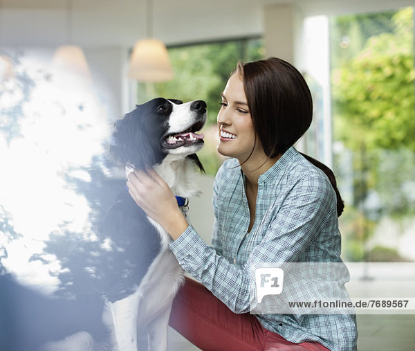 Lächelnde Frau streichelt Hund im Haus