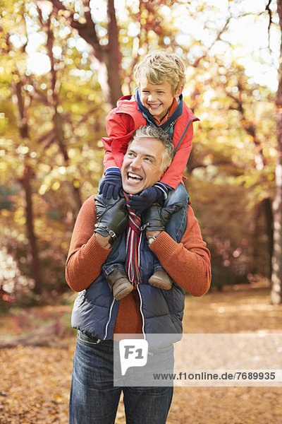 Older man carrying grandson on shoulders in park