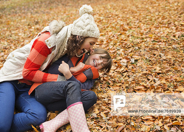 Mother and daughter playing in autumn leaves