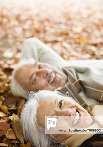 Older couple laying in autumn leaves