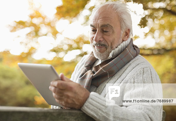 Older man using tablet computer in park