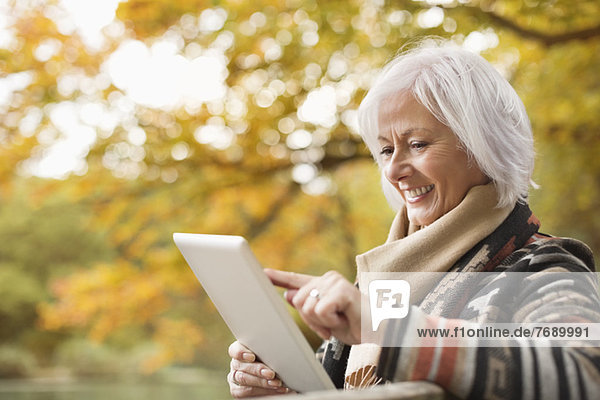 Older woman using tablet computer in park