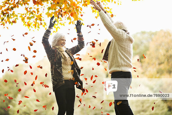 Older couple playing in autumn leaves