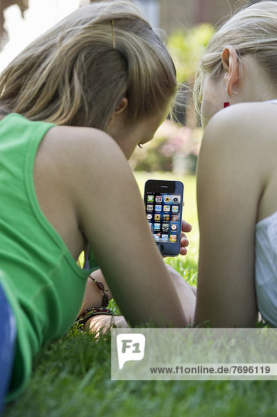 Junge Frauen mit Smartphone liegen auf Gras