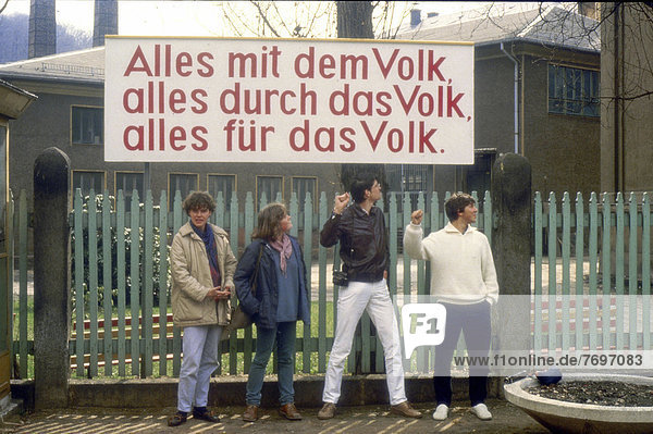 Socialist propaganda sign  Alles mit dem Volk  alles durch das Volk  alles fuer das Volk  German for Everything with the people  everthing by the people  everything for the people  four pupils from a West German high school class on a study trip standing in the front  in April 1985  GDR  German Democratic Republic  Europe