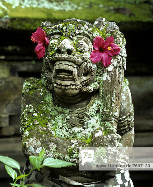 Barong  Kopf aus Stein gemeißelt mit roten Hibiskus-Blüten