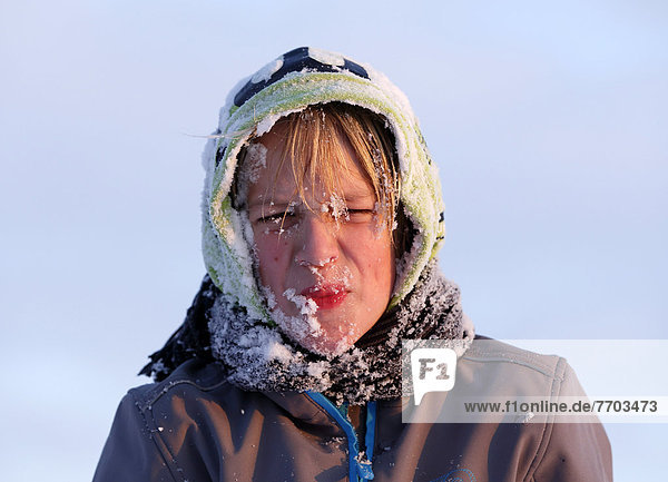 Junge  11 Jahre  mit Schnee im Gesicht und Kapuze  zieht Grimasse