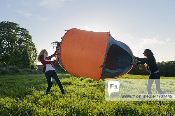 Teenage girls pitching tent in field