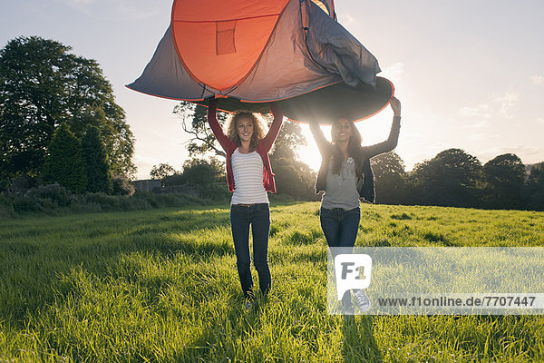 Teenage girls pitching tent in field