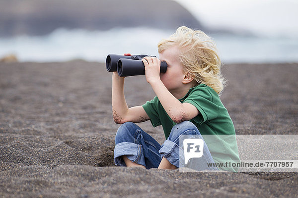 Boy using binoculars on beach