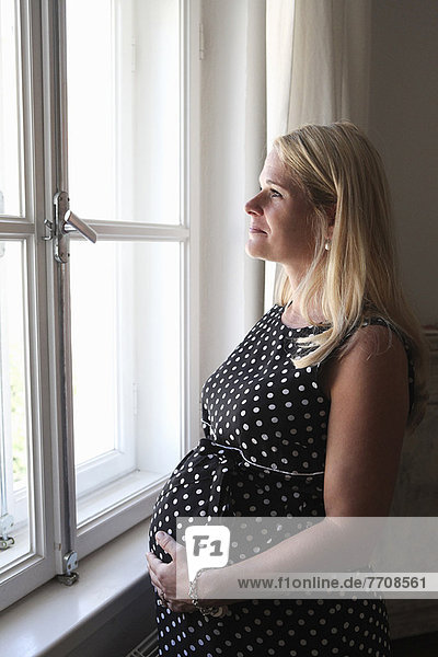 Schwangere Frau lächelt am Fenster