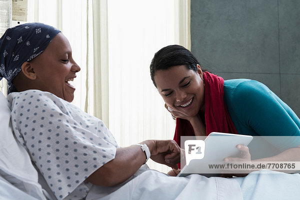 Daughter visiting mother in hospital  showing her digital tablet