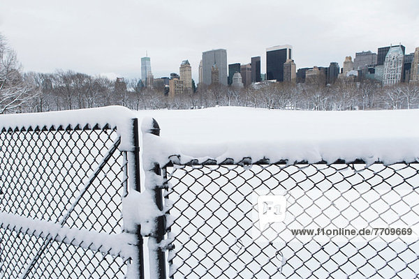 Zaun  verschneiter Stadtpark und Skyline