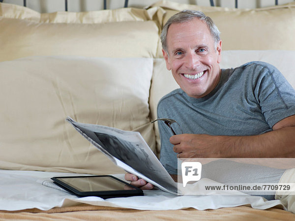 Older man reading newspaper on bed