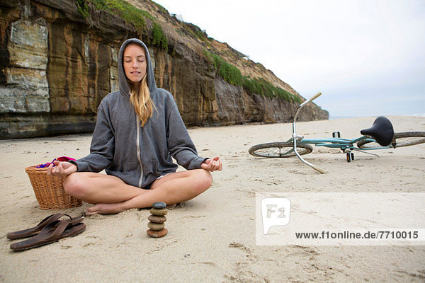 Frau meditiert mit Felsen am Strand