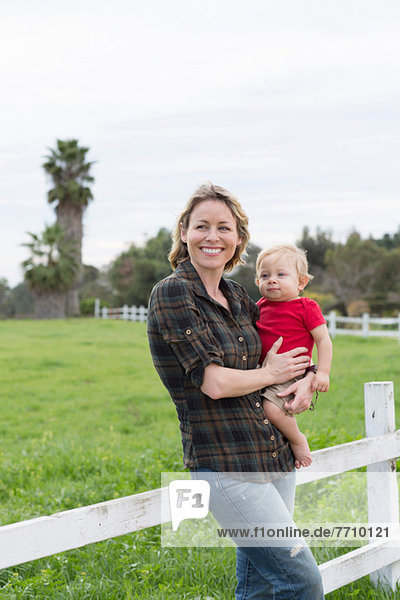 Woman holding son by wooden fence