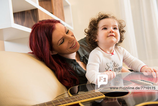 Mutter und Tochter mit Gitarre auf Sofa