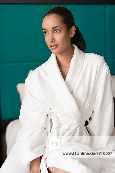 Woman in bathrobe sitting on bed
