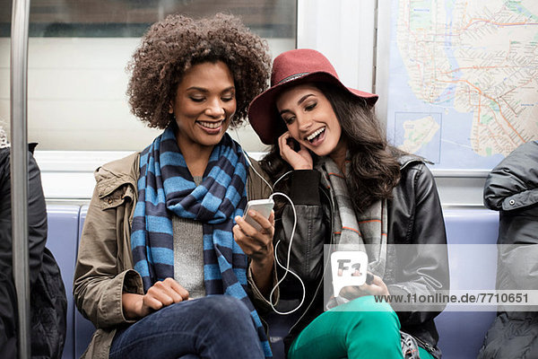 Women sharing earphones on subway