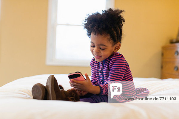 Mädchen spielt mit Handy im Bett