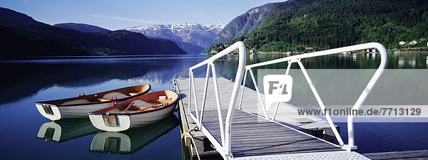 Row Boats By Jetty On Lake By Mountains