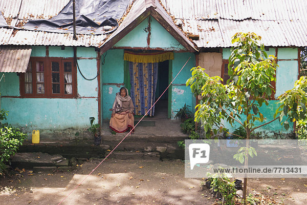 sitzend Frau Wohnhaus Holz Vordach Indien Westbengalen