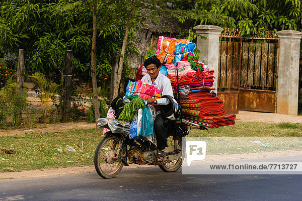 Man riding motorbike loaded with colorful textiles  Cambodia