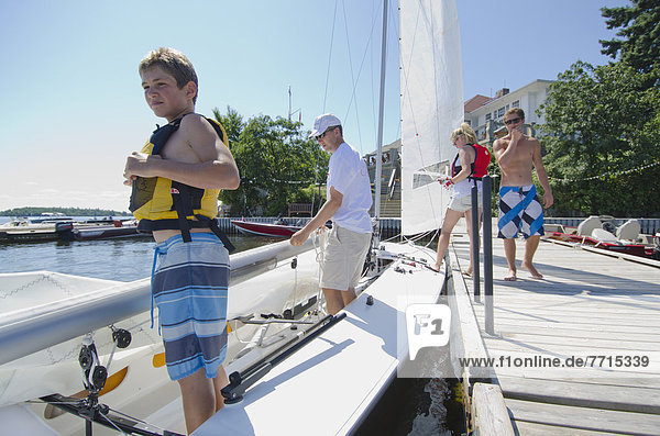 Teenage Boy Wearing A Life Jacket Standing In A Sailboat At The Royal Lake Of The Woods Yacht Club  Kenora Ontario Canada
