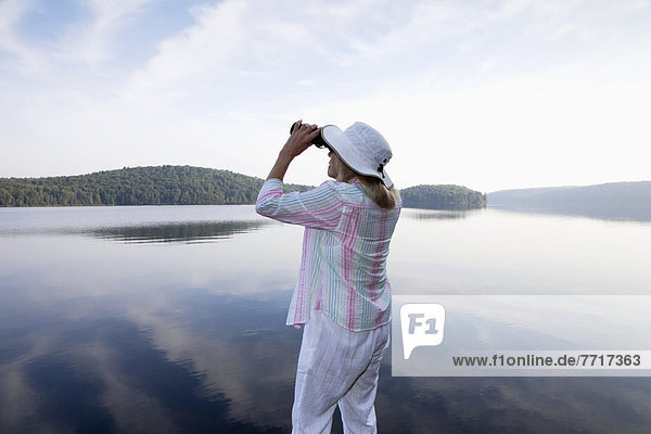 Senior woman looking through her binoculars while standing on her cottage dock in algonquin park Ontario canada