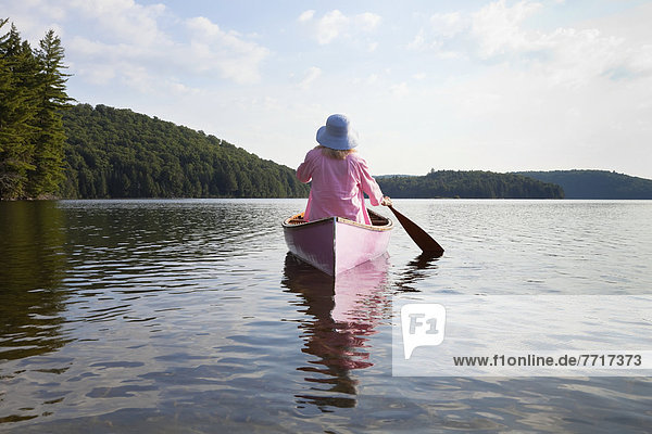 Senior woman dressed in pink and paddling her pink canoe on lake in algonquin park Ontario canada