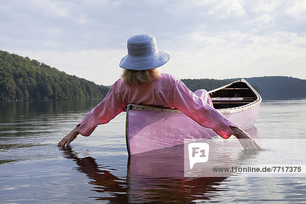 Senior woman dressed in pink and trailing her hands in the water from her pink canoe in algonquin park Ontario canada