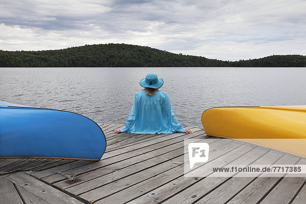 Senior woman sitting on a dock between her canoes under a stormy sky in algonquin park Ontario canada