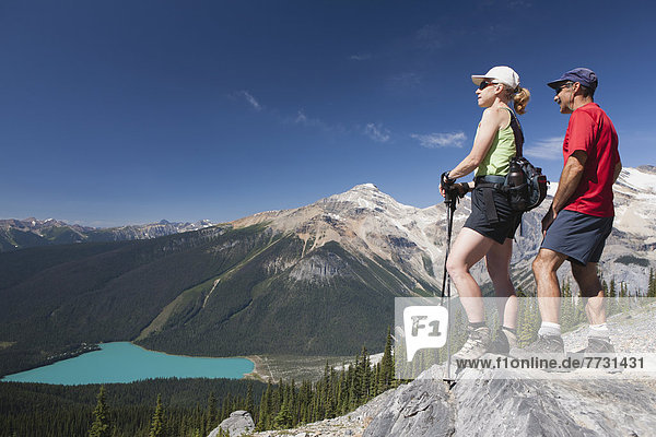 Female And Male Hikers On Top Of Rock Cliff Overlooking Lake Below  Field British Columbia Canada