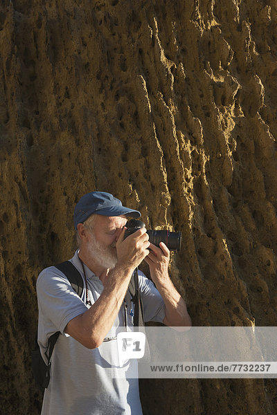 A man standing beside a rock cliff taking a photograph with his camera  andalusia spain