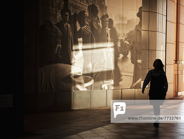 Woman walking by large picture displayed on wall along walkway  Tokyo  Japan