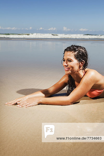A Woman In A Bikini Lays On The Sand Of A Beach At Low Tide  Gold Coast Queensland Australia