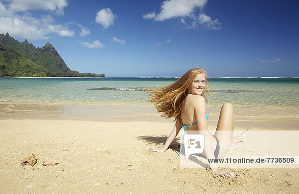 A young woman sitting in the sand along the ocean at the coast  kauai hawaii united states of america