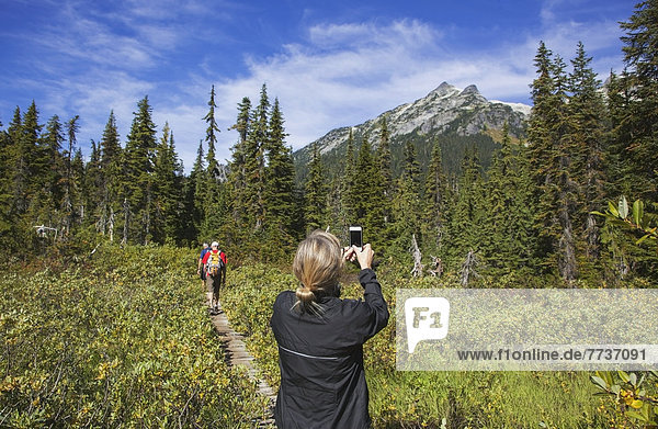 A woman takes a photograph of the mountains on a hiking trail Whistler british columbia canada