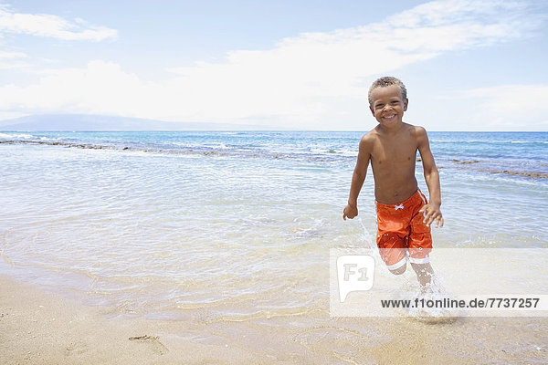 A young boy runs and plays in the shallow water of the ocean Hawaii united states of america